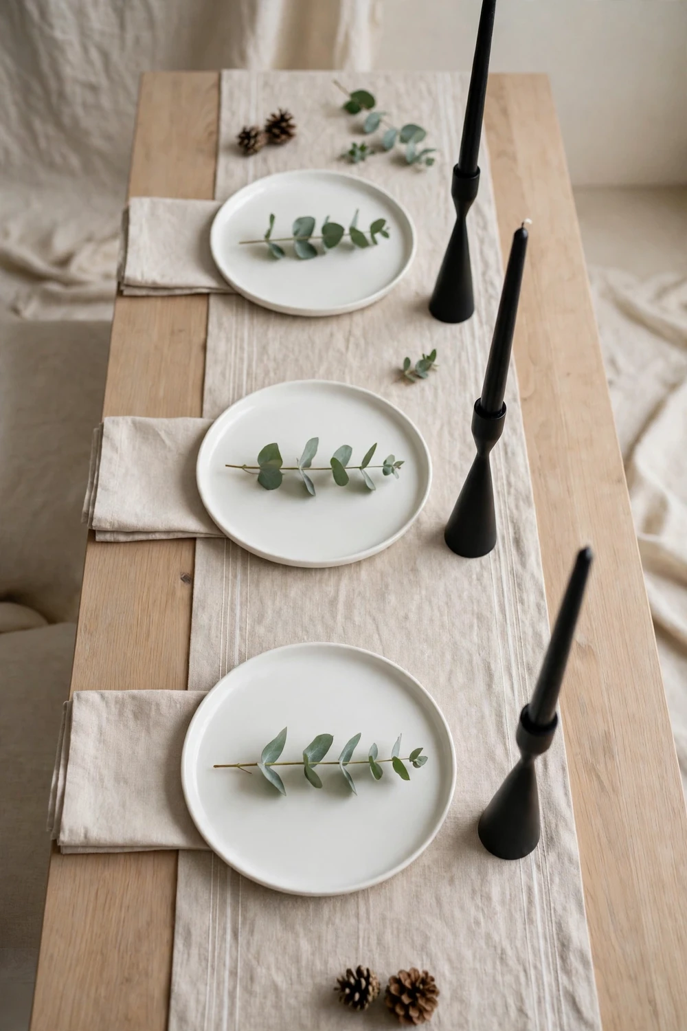 Modern minimalist Christmas table with clean white plates, eucalyptus sprigs and black candle holders